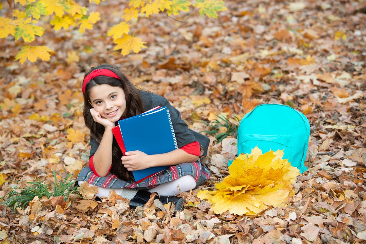 Daycare child with autumn leaves and books